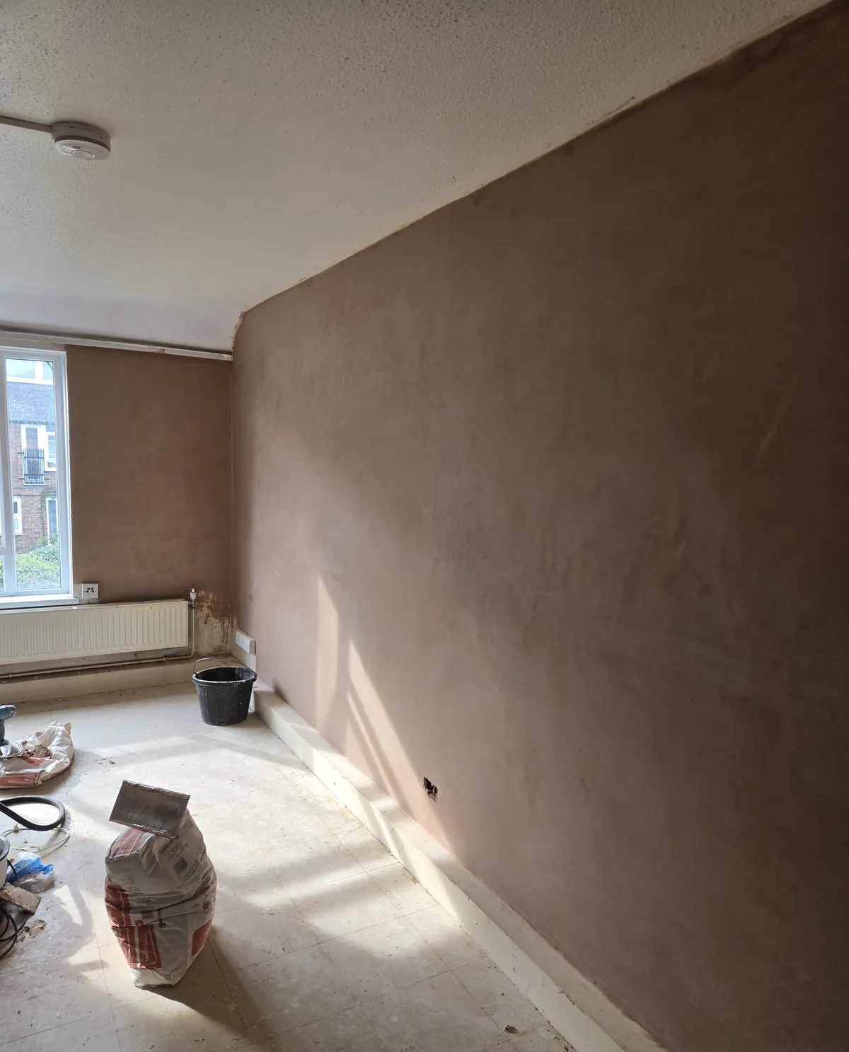 A freshly plastered wall drying in the sunlight, with materials ready for the next stage